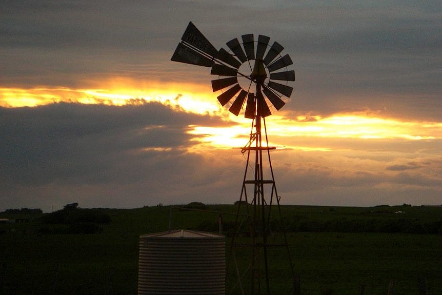 The sun sets behind a windmill on a rural property.