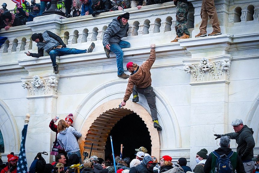 Three men climb up a marble wall as a crowd gathers below