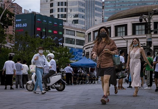 在上海街头，行人走在显示最新经济和证券交易所子信息的大屏幕前。