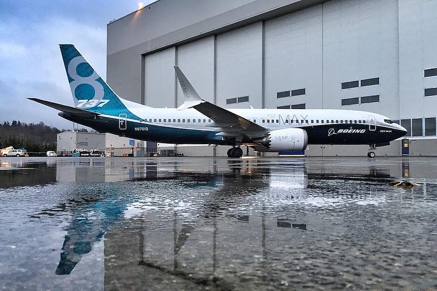 A jet in Boeing blue colours is parked on icy tarmac in front of a beige air hangar.
