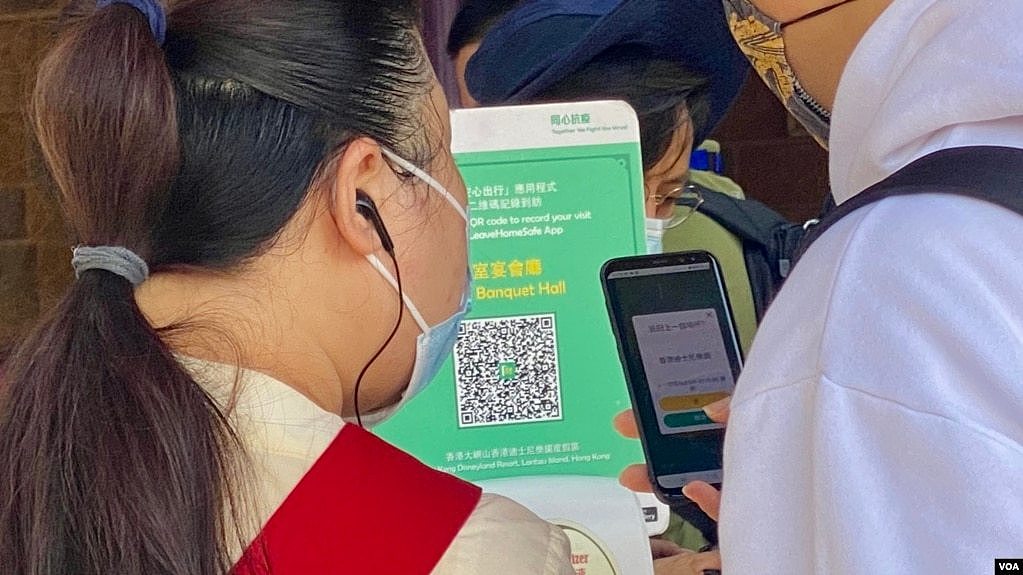 一名香港市民(白衣者)正准备使用防疫手机应用程式“安心出行”进入一间餐厅用膳，身旁的餐厅职员检视使用者是否有准确扫瞄餐厅入口的二维码 (美国之音/汤惠芸)