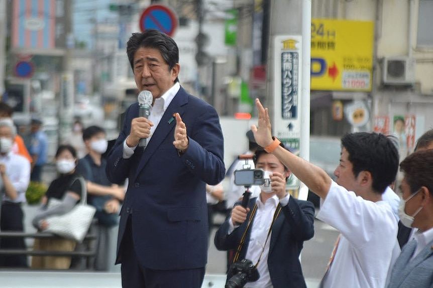 Dressed in a navy suit, Shinzo Abe stands on an intersection with a microphone in his hand, campaigning for an LDP candidate