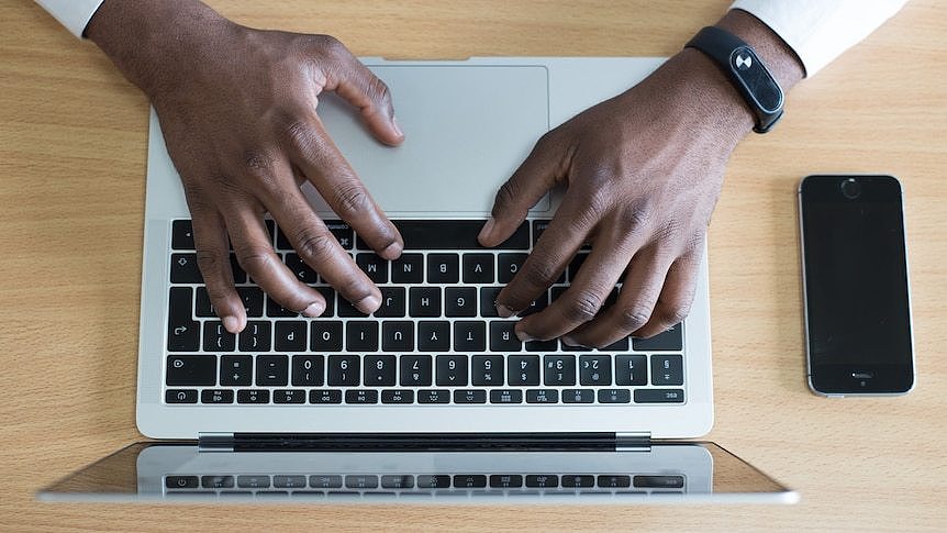 A pair of hands using a laptop. A smartphone sits next to the laptop.