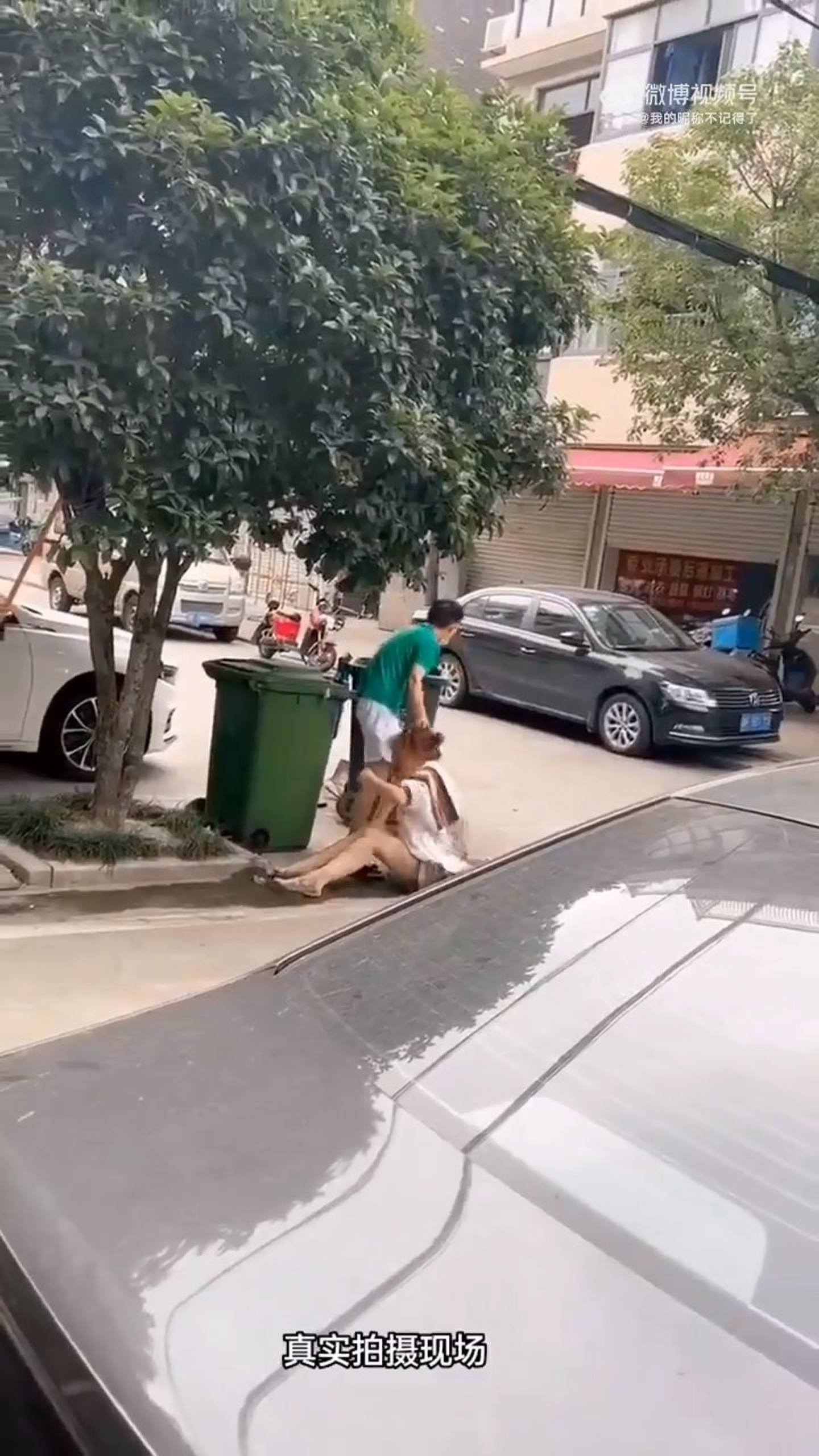 绿色男子抓着女子头发，试图强行把她塞进旁边的垃圾桶，女子不断挣扎反抗。 （影片截图）