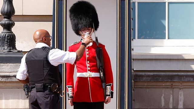 A member of the Queen's Guard wearing a bearskin hat receives water to drink during the hot weather, outside Buckingham Palace in London