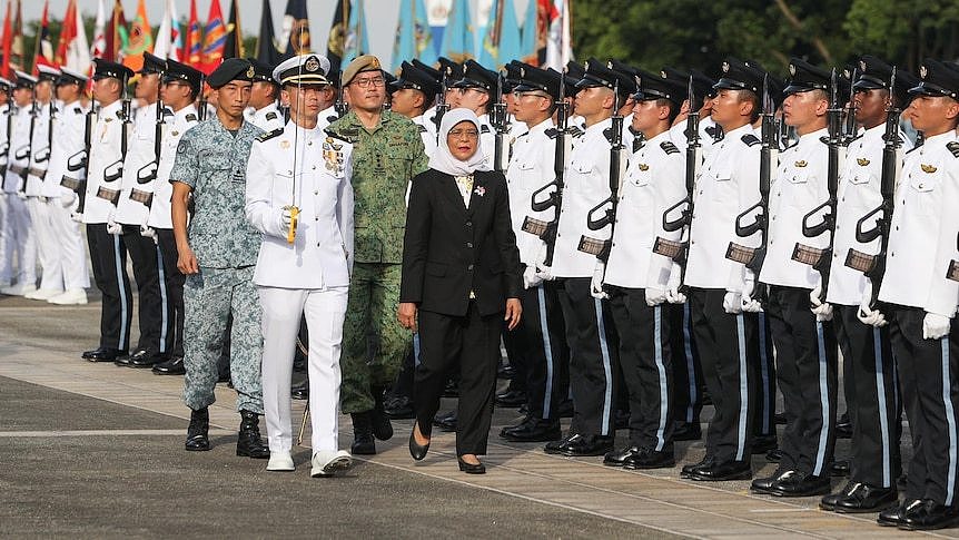 A middle-aged Muslim woman walks with three men in military uniform as she inspects police officers dressed in white 