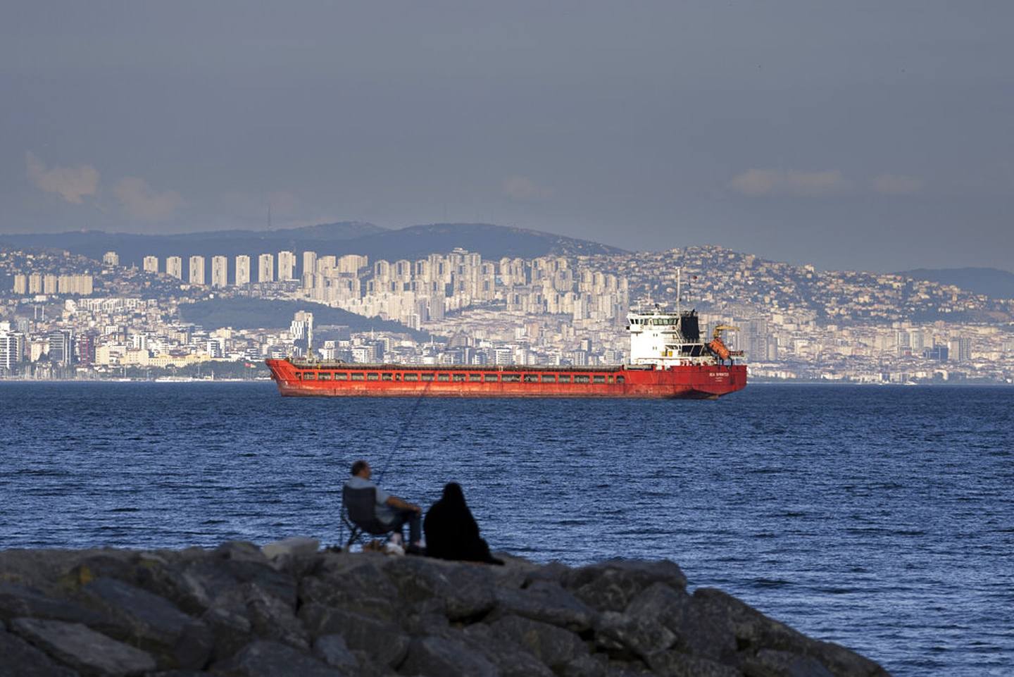 乌克兰：图为2022年7月13日，土耳其伊斯坦堡，有一家人坐在马尔马拉海（Sea of Marmara）旁的岩石上，看着一艘已下锚、等待驶过博斯普鲁斯海峡（Bosporus Strait）的货轮。 博斯普鲁斯海峡又称伊斯坦堡海峡，是连接黑海和马尔马拉海的一条狭窄水道。 （AP）