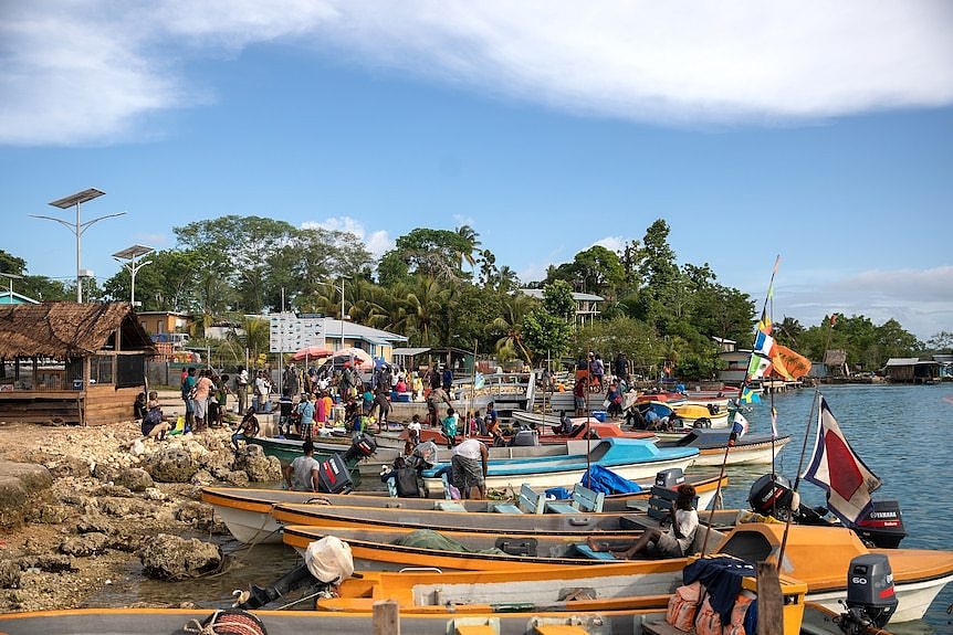 在一个岩石海滩的岸边有许多小船。几十个人在船的周围和船上站着、坐着。