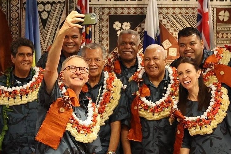 Anthony Albanese holds a phone as members of the Pacific Island Forum, all wearing traditional dress, pose for a group selfie