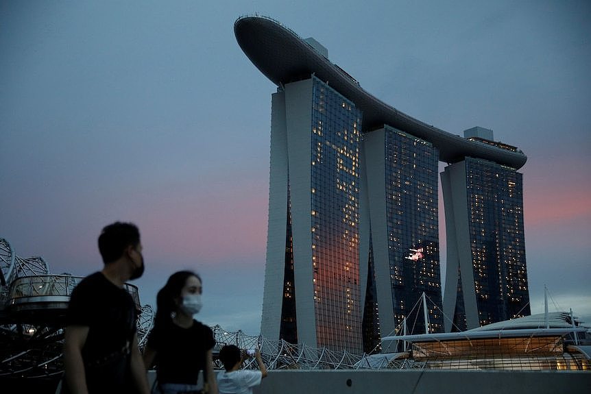 Two people are seen in the foreground, with the huge three-pronged building of the Marina Bay Sands hotel in the background. 
