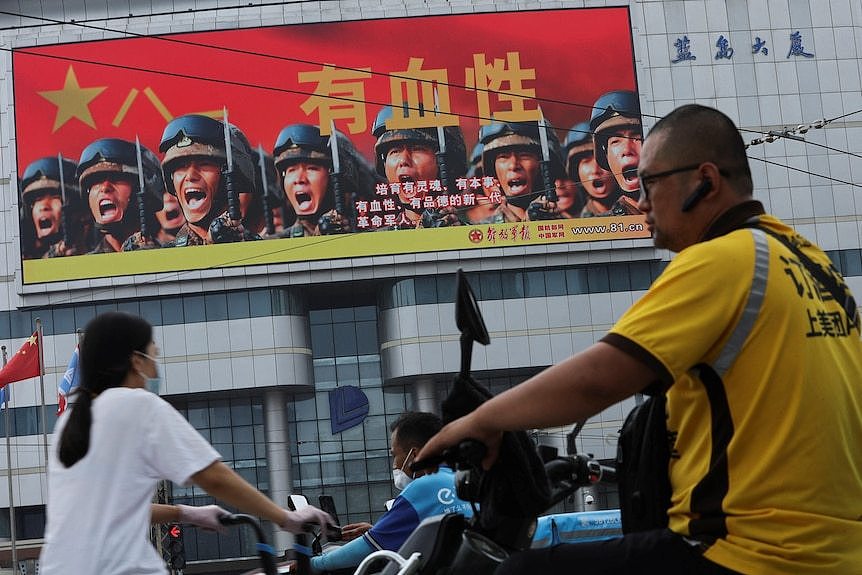 一名外卖配送员骑车经过北京市中心的一块大银幕，屏幕上播放着解放军的视频