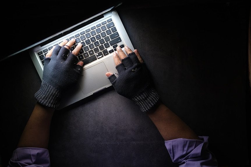 A pair of hands wearing fingerless gloves using a laptop computer in a dark room.