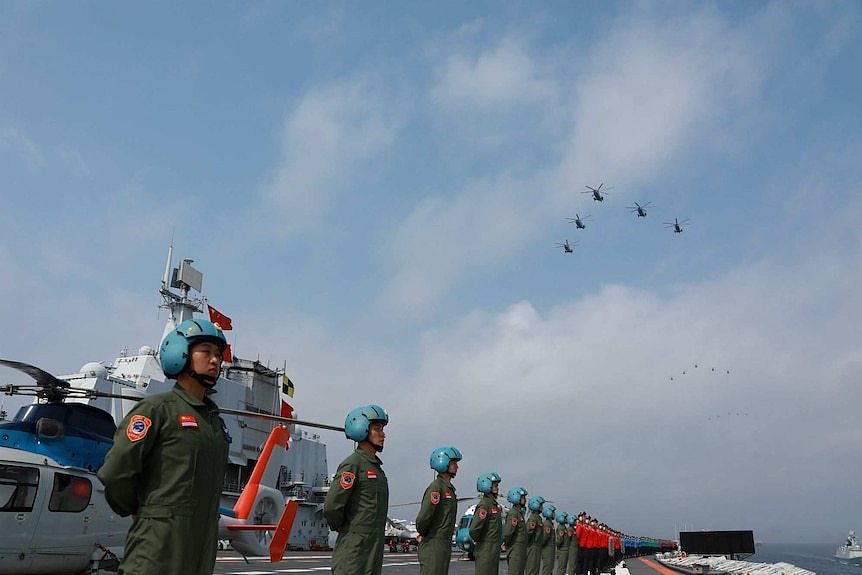 Navy personnel of Chinese People's Liberation Army stand in line, there are military aircrafts above and behind them.