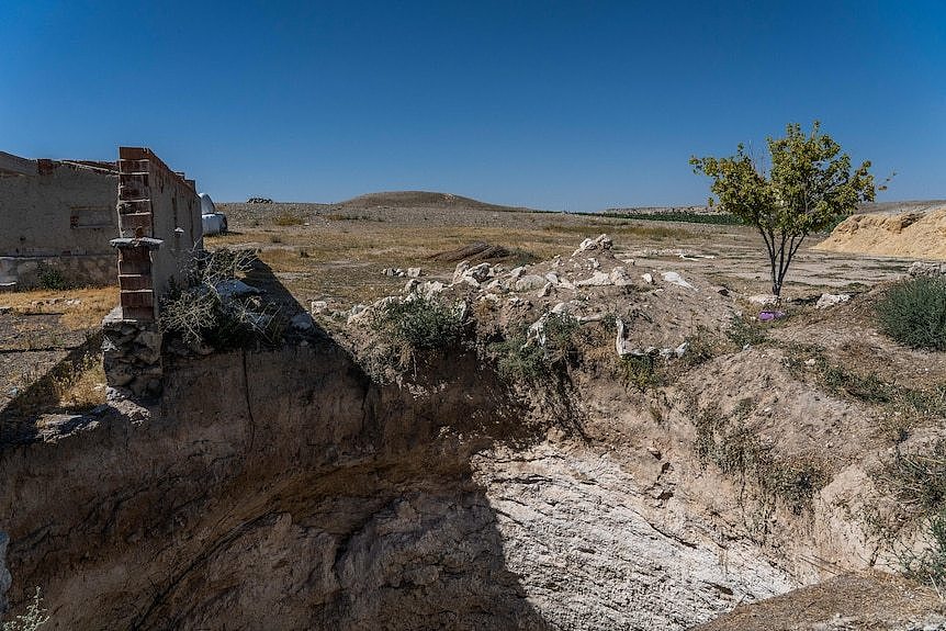 A large sinkhole is seen next to a crumbling structure on a wide open landscape