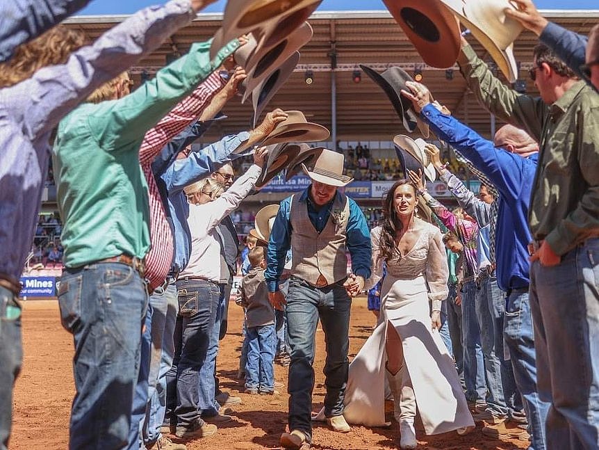 newlywed couple walks through cowboy guard of honour on rodeo arena