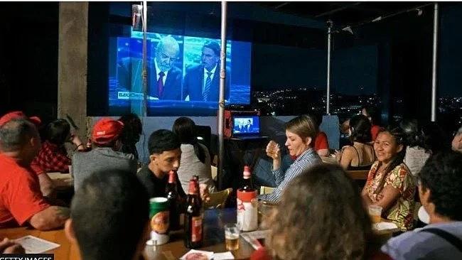 巴西民众观看电视辩论，电视左边的卢拉，右边的是博索纳罗。