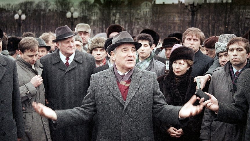 A man (Mr Gorbachev) stands at the foreground of a mass of people, gesturing with his hands while he speaks. 