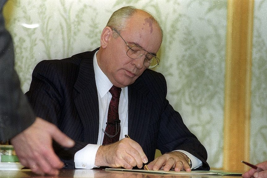 身穿西装的戈尔巴乔夫坐在办公桌前签署了辞呈。