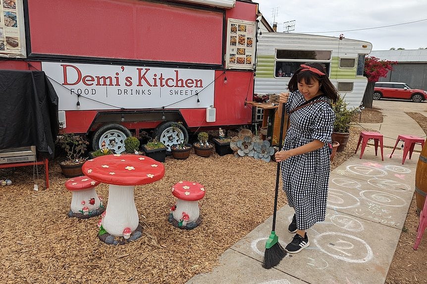 一名短发女性站在一辆红色餐车旁，周围拜访者小蘑菇形状的座椅