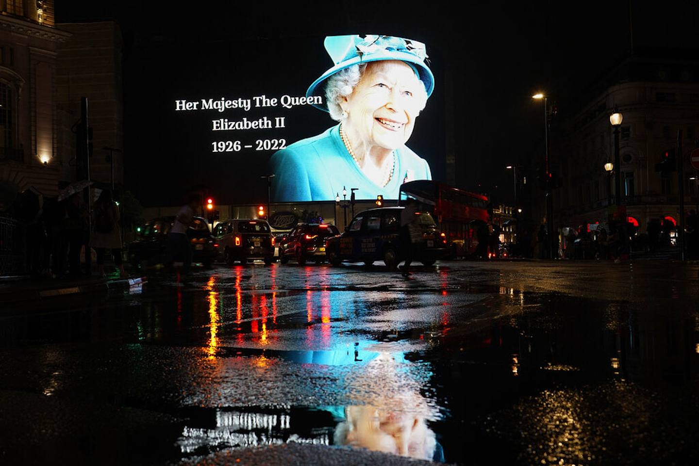 英女王伊利沙伯二世逝世：圖為2022年9月8日，女王去世後，倫敦皮卡迪利圓環（Piccadilly Circus）一個大型熒幕播映出女王的遺照，並在下雨後的地面投下倒影。白金漢宮8日說，她當天下午在巴爾莫勒爾堡去世。白金漢宮同日發布新國王的聲明說，女王的辭世「對我和我家庭的所有成員來說是最悲傷的時刻。」（AP）