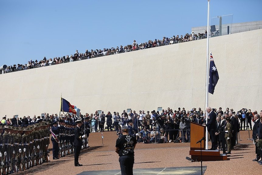 A row of onlookers leans over the ramps of Parliament House as the governor-general stands at a podium below.