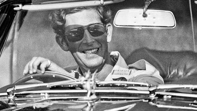 1975年温莎马球场，阿斯顿马丁跑车驾驶座上戴着墨镜、满脸笑容的查尔斯三世