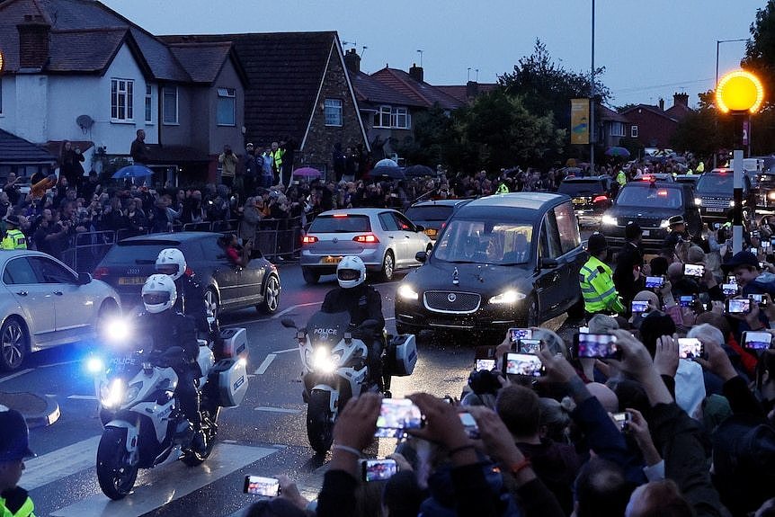 A hearse carrying the coffin of the Queen drives down a road.