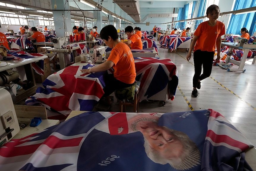 Workers that are wearing orange t-shirts are seen sowing British flags in a factory.