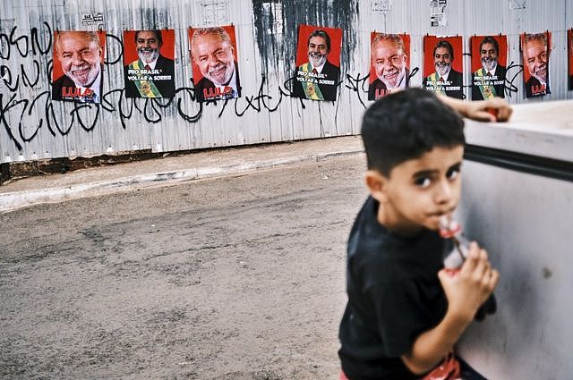 一个巴西儿童在街上喝可口可乐，后面是卢拉的竞选画报