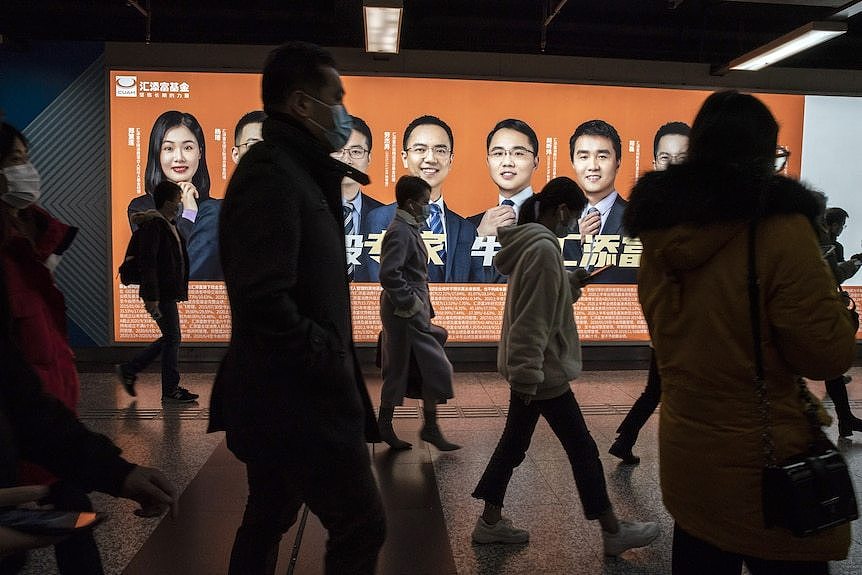 Chinese commuters walk past a billboard in a subway