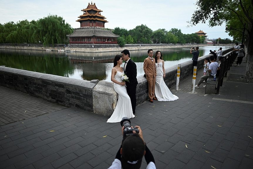 Two couples in wedding outfits post for photos in front of a canal.