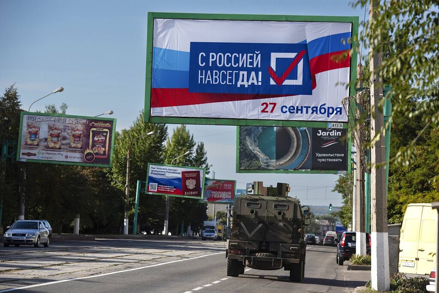 烏克蘭局勢：俄軍在烏克蘭控制的盧甘斯克於23日舉行公投，要求選民決定是否讓該區成為俄羅斯的一部份。圖為2022年9月22日，一部軍車駛在盧甘斯克街道上，它的上方有一片大型廣告牌，寫有「與俄羅斯永遠在一起，9月27日」的字樣。除了盧甘斯克，頓涅茨克、赫爾松及扎波羅熱都舉行入俄公投。（ AP）