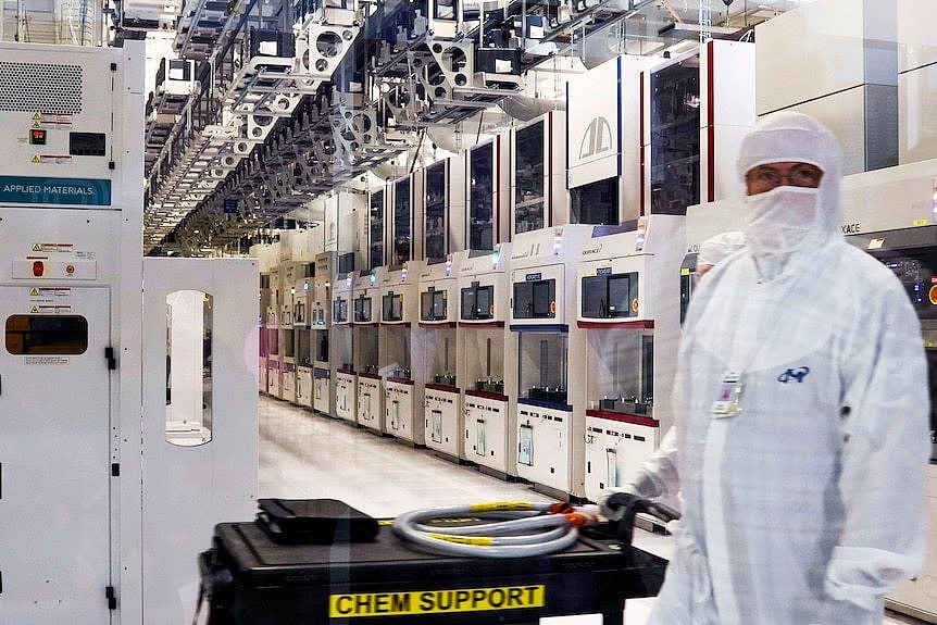 A person in white full body PPE stands in a row of white high tech manufacturing devices.
