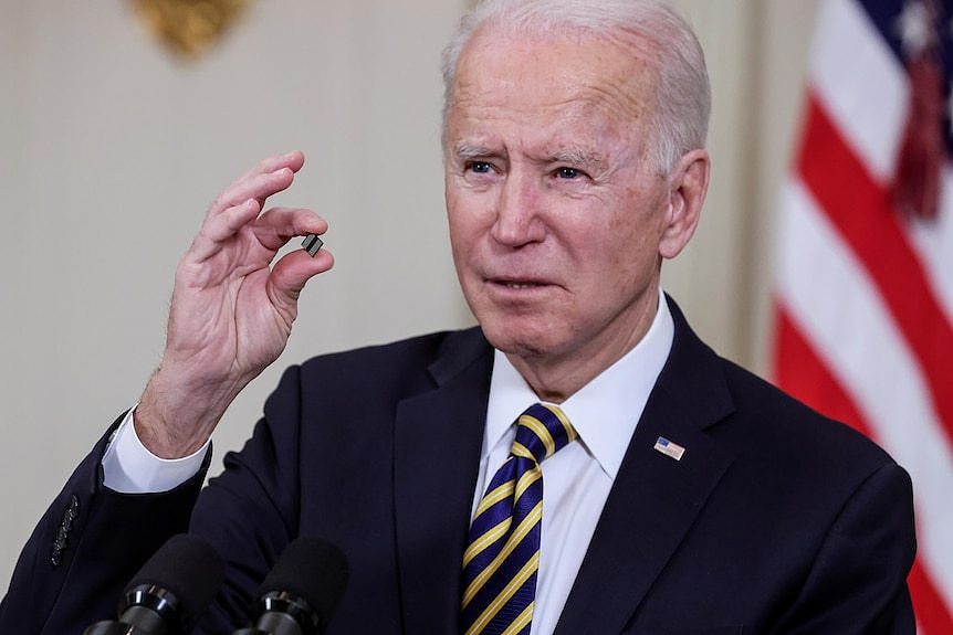 Joe Biden holds up a tiny little computer chip between his fingers 