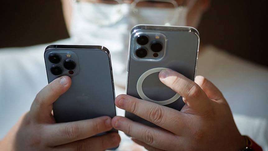 A man in a mask holding two iPhones. 