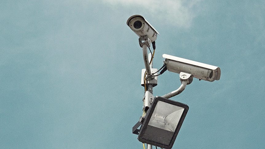 Two security cameras against a grey sky.