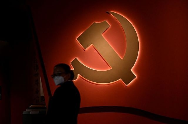 在北京国家博物馆举行的以中国共产党为主题的展览中，一名妇女站在党徽前。