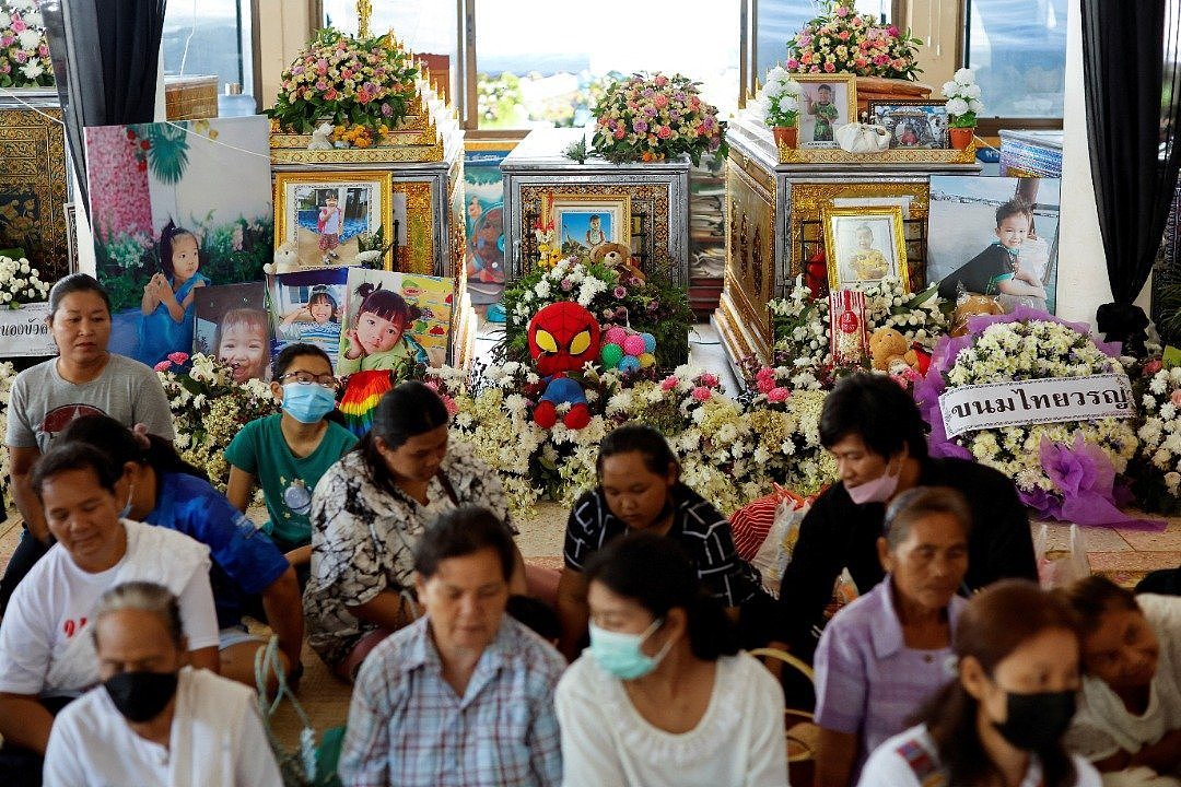 在乌泰沙旺镇枪击案受害者的葬礼上，家属坐在遇害孩子的棺材旁，棺材旁除了摆放死者遗照，也堆满鲜花和玩具。（图取自路透社）