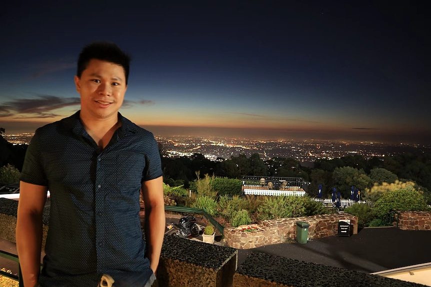 一名亚洲男子站在阳台生背后是夜景