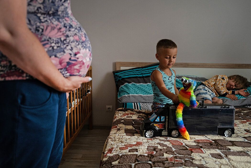 43岁的维多利亚托着肚子，她2岁的女儿和另一位代孕妈妈的儿子在床上玩耍。