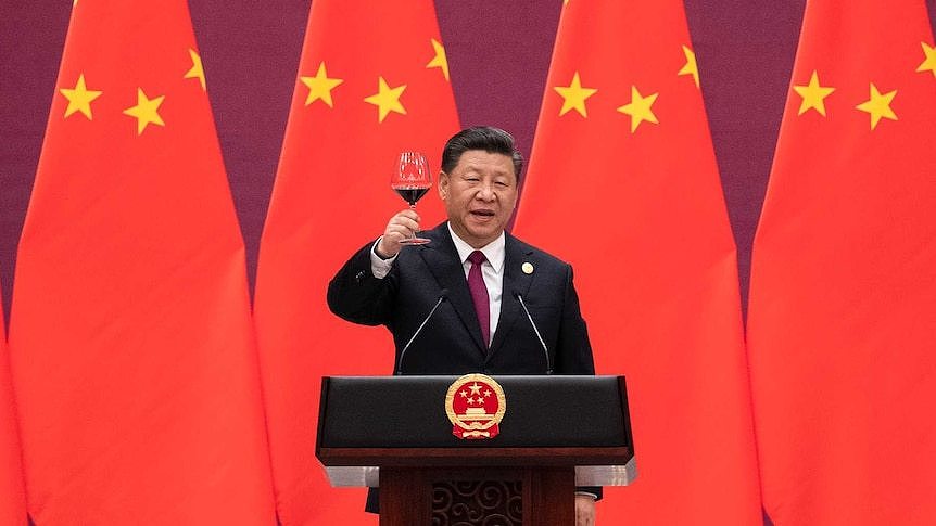 Xi Jinping stands in front of nine large Chinese flags as he toasts a glass of red wine standing behind an official lectern.