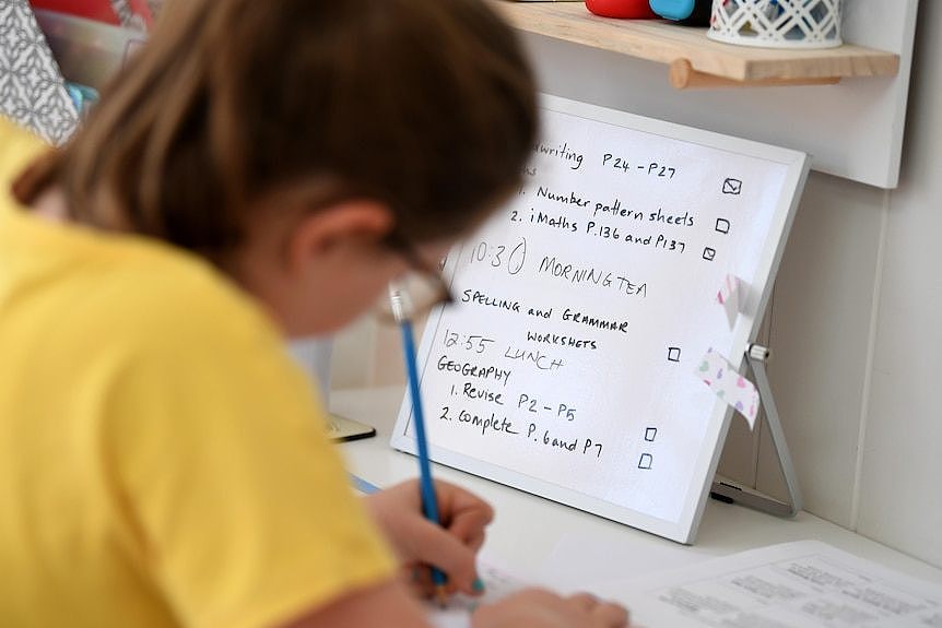 a young female student holding a pen and writing on a desk at home