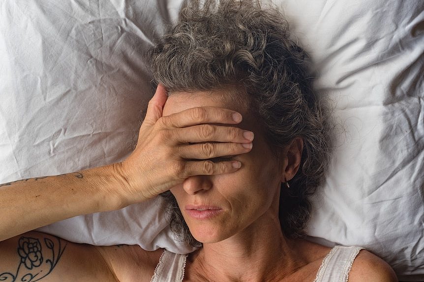 一位女性躺在床上，手遮住了她的眼睛
