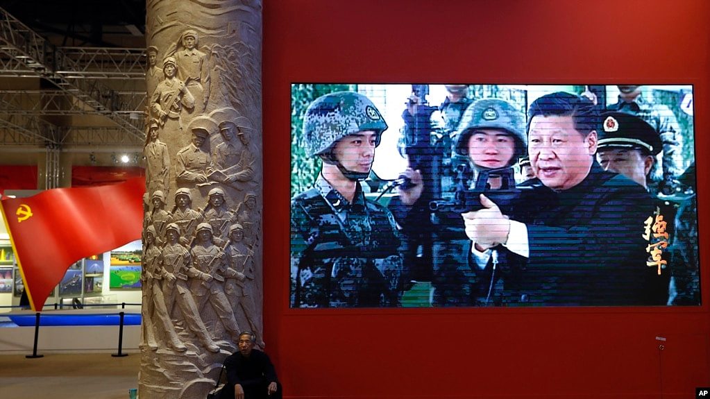 资料照片：2017年10月23日，一名男子在北京的一个视频屏幕旁边休息。视频显示，中国国家主席习近平在北京展览馆举行的一场展览上拿着一支步枪。（美联社照片）