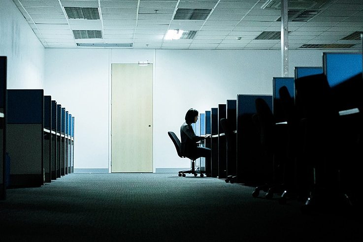 A woman sits at a computer in a dark room.