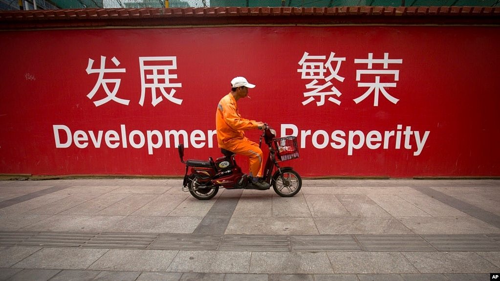 在北京市中心的一条街道上，一名维修工人骑着摩托车经过用中英文书写的“发展”和“繁荣”的标语（2015年7月15日）。