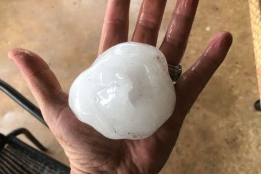 A woman holds a hail stone the size of a cricket ball in her hands. 