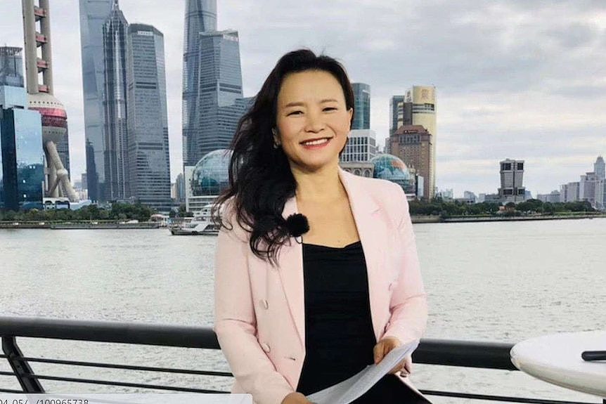 Journalist Cheng Lei is seen smiling while seated with the Shanghai waterfront in the background.