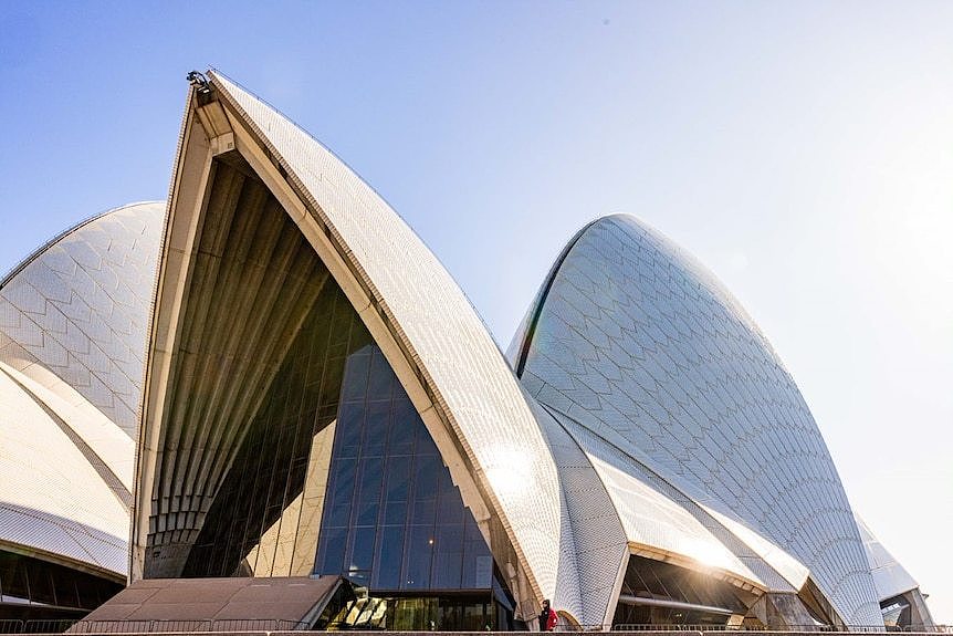 White tiled sails of the Sydney Opera House peak up into a clear blue sky.