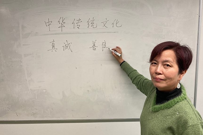 A woman stands in front of a whiteboard with Chinese on it. 